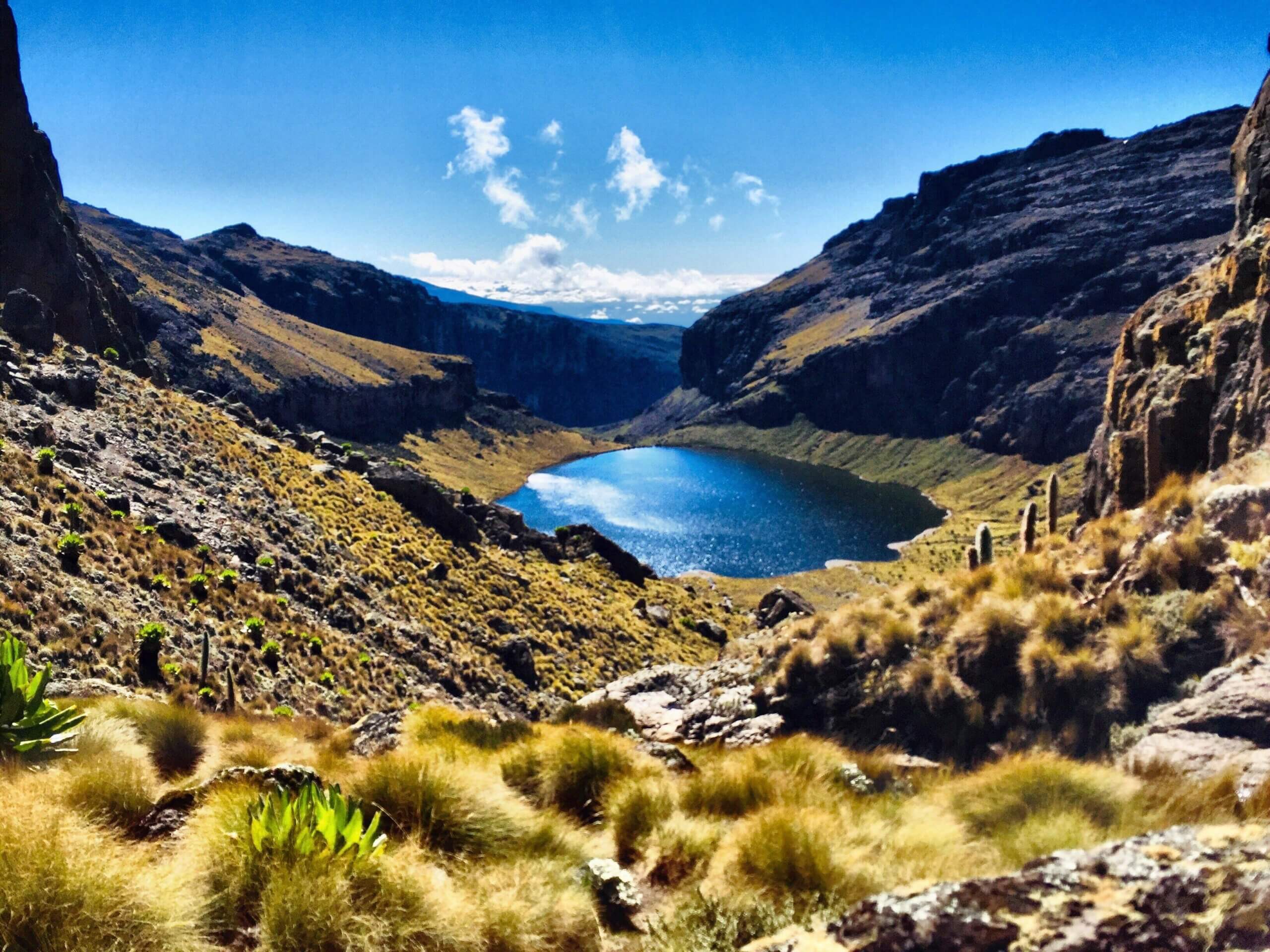 A view of Lake Michaelson sitting in a deep valley on Mount Kenya, surrounded by steep rocky cliffs and high-altitude terrain along the Chogoria Route.